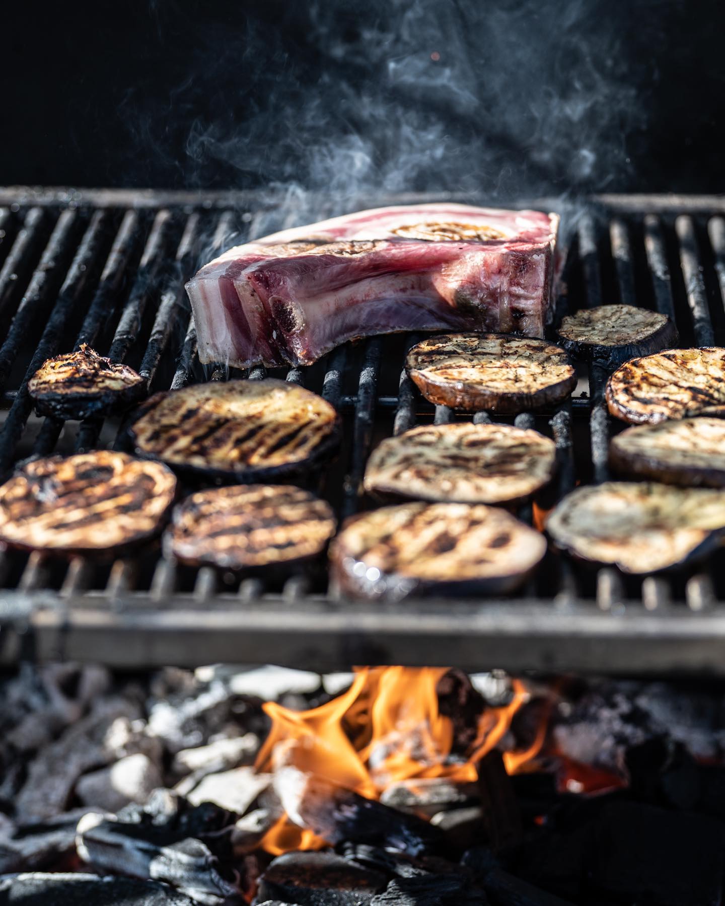 Aubergines et pièce de viande sur la grille du brasero, foyer ouvert